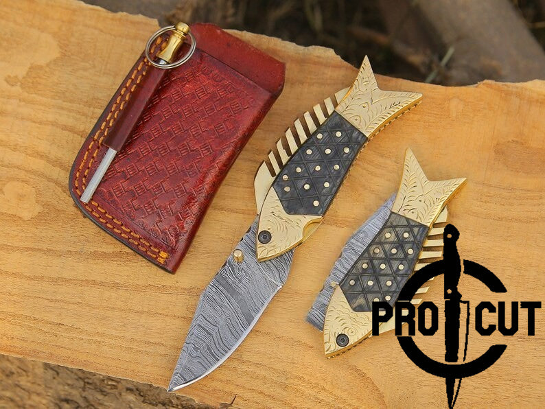 Two fish-shaped knives with decorative handles on a wooden surface, next to a red leather case. 'Pro Cut' logo visible.
